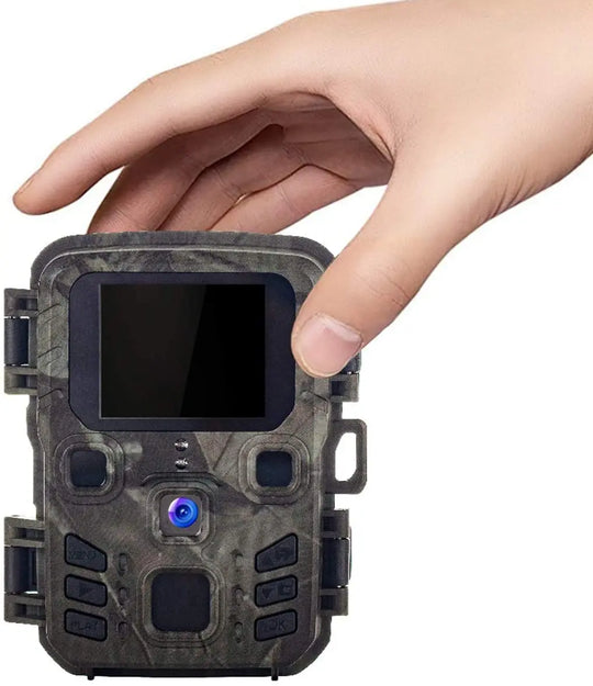 Compact camouflage trail camera held in one hand with front display and central lens for wildlife monitoring and outdoor security