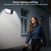 GPS outdoor wall light with built in camera illuminates a woman walking past a house, illustrating automatic motion activated lighting for added safety