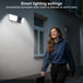 GPS outdoor wall light with built in camera illuminates a woman walking past a house, illustrating automatic motion activated lighting for added safety